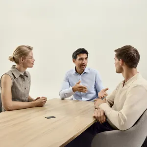 PLAUD Note Pro voice recorder on a meeting table beside three people in discussion