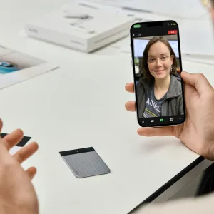 PLAUD Note Pro recorder beside a smartphone on a desk during a video call meeting