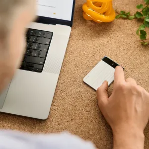 PLAUD Note Pro voice recorder with AI transcription on a desk beside a laptop, being touched