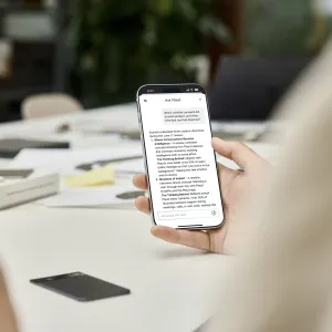 PLAUD Note Pro voice recorder beside a phone showing the Ask Plaud app in a meeting room