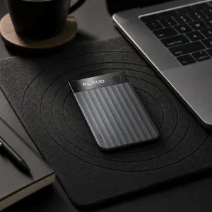 PLAUD Note Pro transcription device on a desk mat beside a laptop, notebook and mug