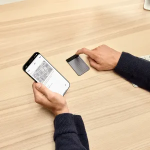 Grabadora de voz con IA PLAUD Note Pro sobre un escritorio, con una persona pulsando el botón superior junto a la app Plaud en un smartphone.