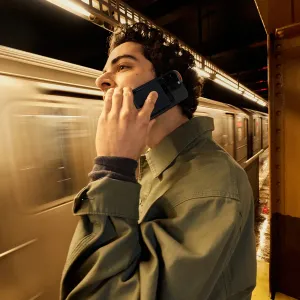 Grabadora de voz con IA PLAUD Note Pro adherida a un smartphone durante una llamada en un andén de metro