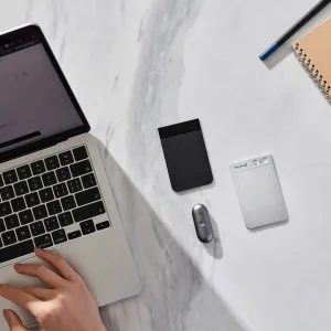 Grabadora de voz con IA PLAUD Note Pro sobre un escritorio, junto a un portátil, un cuaderno y un bolígrafo, con un diseño magnético plateado