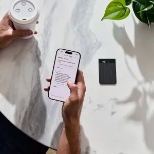 PLAUD Note Pro, grabadora de voz con IA negra, junto a un smartphone que muestra notas y transcripción
