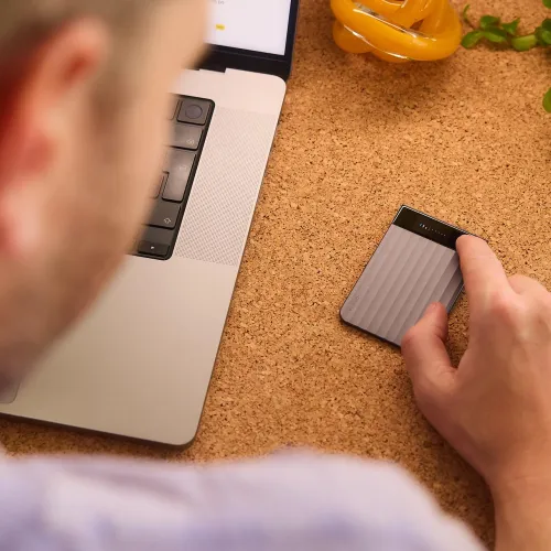 PLAUD Note Pro compact AI transcription device on a desk beside a laptop, with indicator lights visible.